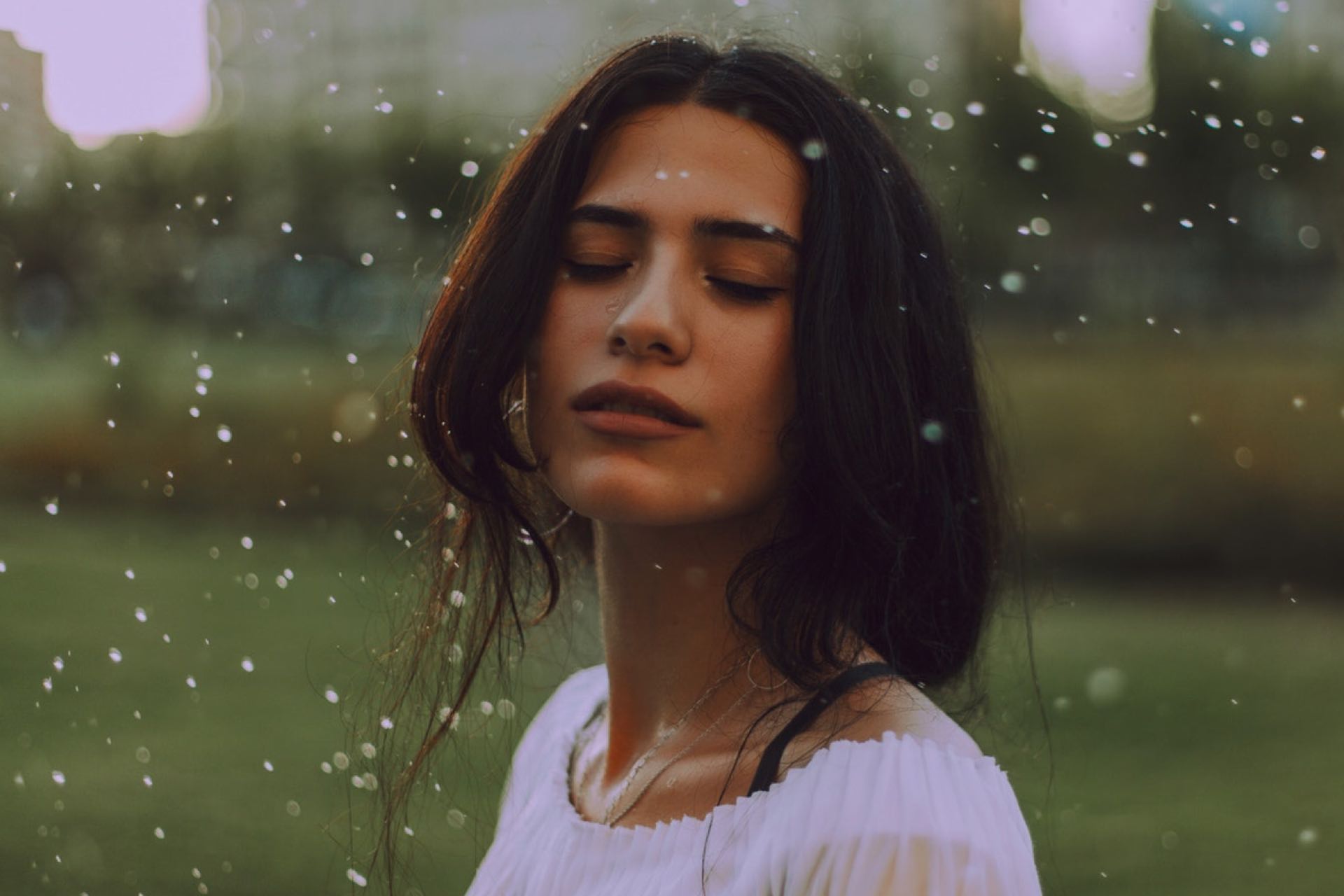 Eine junge Frau umgeben von Wassertropfen. Ihre Augen sind geschlossen, sie genießt und erfrischt ihre makellose Haut.