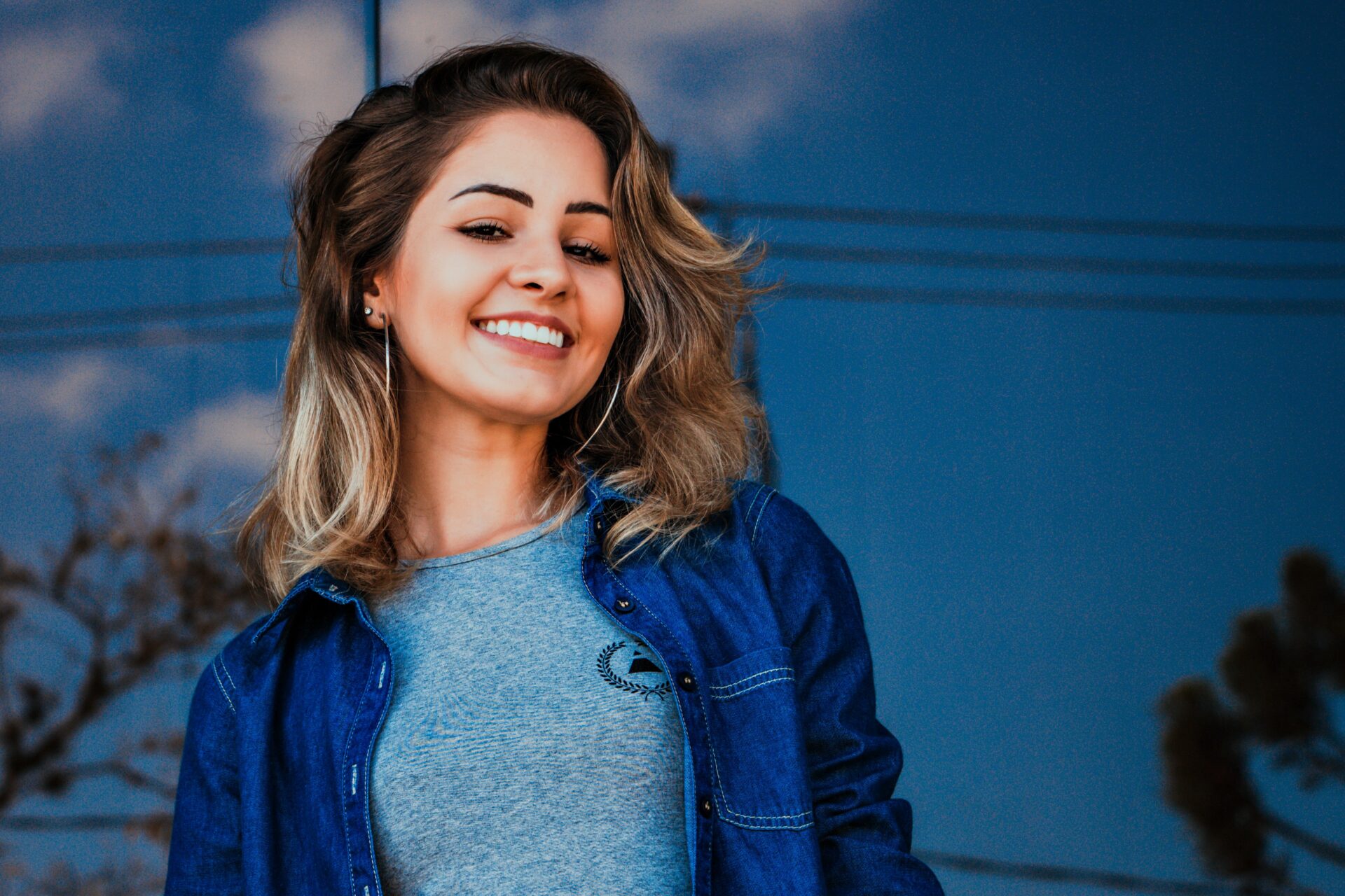 Blonde Frau in Jeansjacke lächelnd vor einem blauen Hintergrund